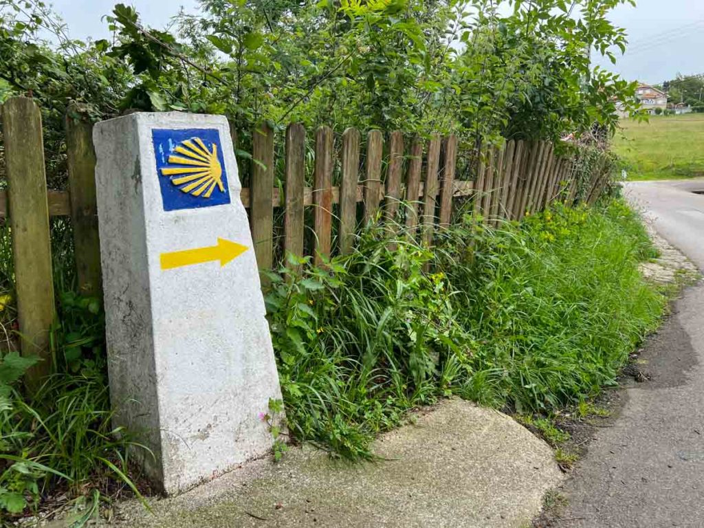 Camino Primitivo way marker, with fence and bushes.