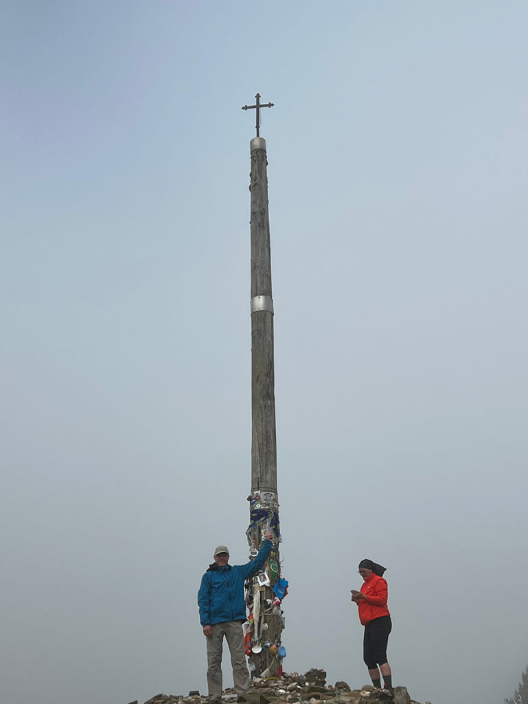 Bruce Cass at Cruz de Ferro, large cross and two pilgrims.